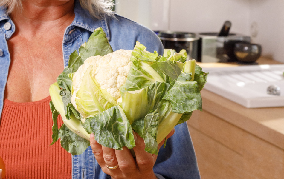 Frau hält Blumenkohl mit Blättern in ihrer Hand